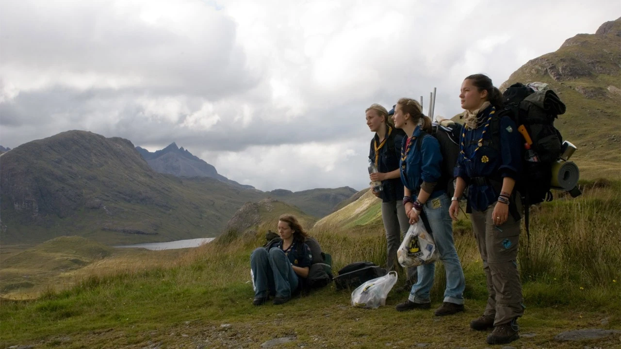 Vier Pfadfinderinnen stehen auf einem Grashügel mit Bergen im Hintergrund